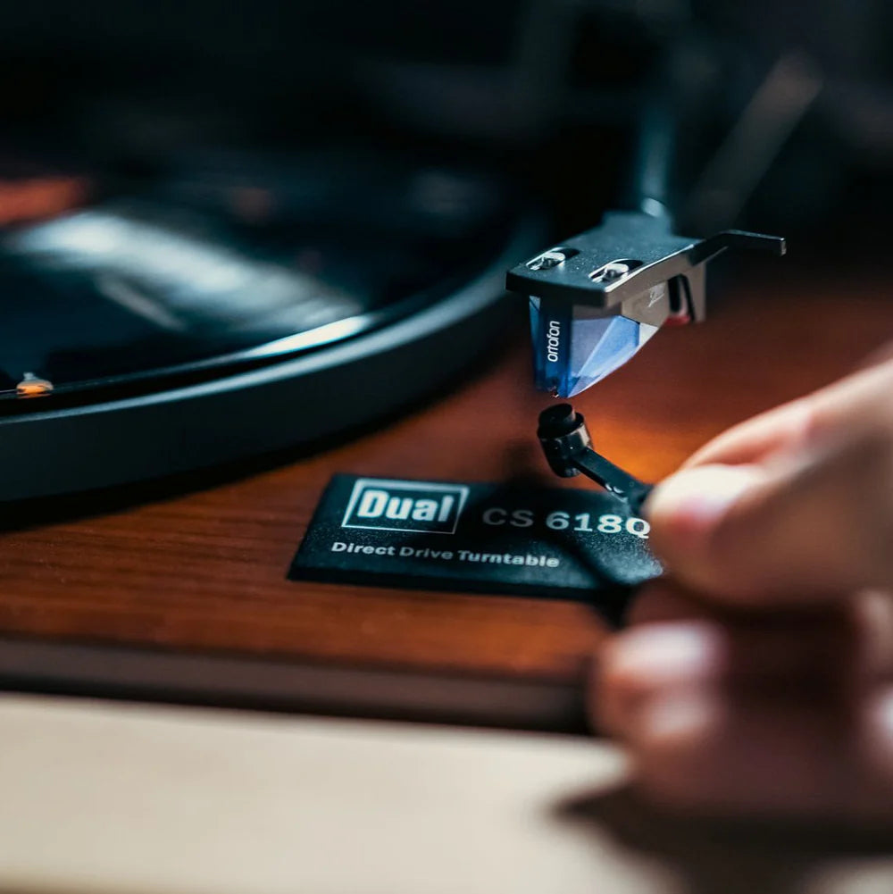 Person adjusting a Dual CS 6180 turntable cartridge on a wooden turntable.